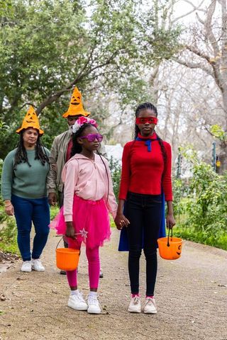 African american girls trick-or-treating with parents wearing pumpkin hats in neighborhood