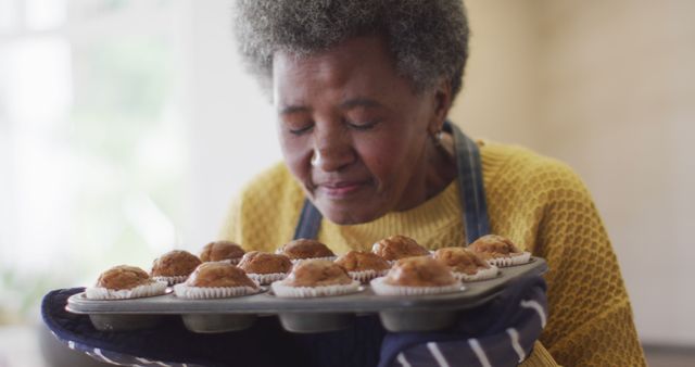 Image of happy senior african american woman holding and smelling tray of freshly baked cup cakes. Retirement, domestic life, health and happiness concept digitally generated image.