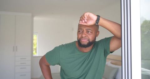 Contemplative african man leaning on sliding door, reflecting in bright bedroom interior