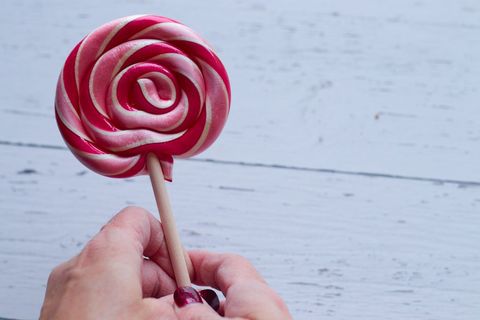 Hand holding pink and white swirl lollipop over weathered white wooden table, candy close-up
