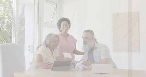 Multigenerational family sharing memories with tablet and printed keepsake, smiling at table