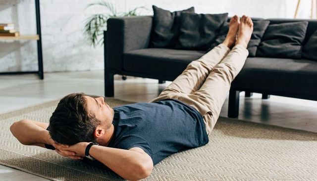 Young man lying on rug with legs on sofa, resting in modern minimalist living room