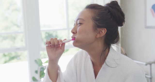 Young woman brushing teeth in bathroom wearing white robe - Download Free Stock Images Pikwizard.com