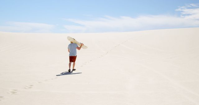 Man walking on sand dunes with snowboard under blue sky - Download Free Stock Images Pikwizard.com