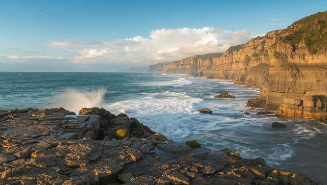 Sunset cliffside coastline with crashing waves and rocky intertidal platform, sea spray