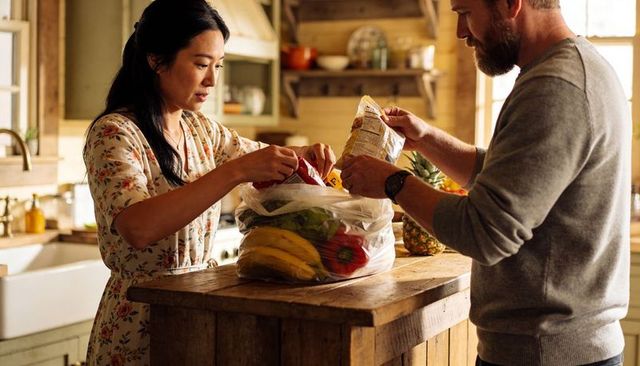 Couple unpacking groceries at rustic farmhouse kitchen island, sorting fresh produce
