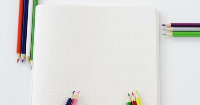 A blank notebook lies open with colorful pencils arranged around it, with copy space. Ideal for back-to-school themes, this setup suggests creativity and the start of a new project.