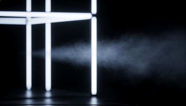 Glowing led tubes forming geometric frame in foggy dark studio with reflective floor