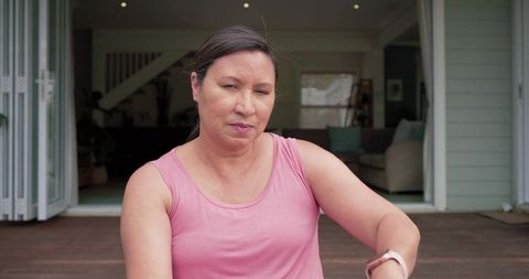 Mature woman on home deck wearing smartwatch and pink tank, relaxed lifestyle