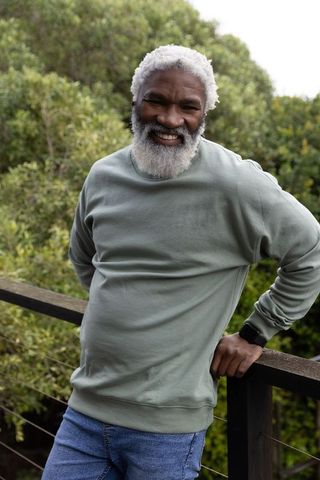 Senior african american man smiling on deck leaning on railing wearing sweatshirt and smartwatch