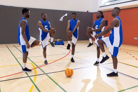 African american basketball team stretching on indoor court warming up for game