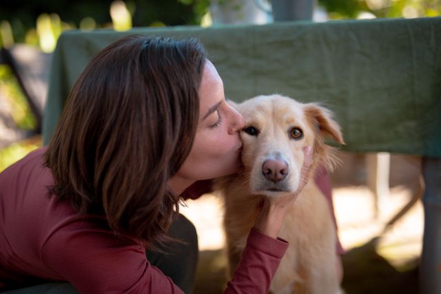 Caucasian woman showing affection by kissing her dog on a patio. Ideal for themes of pet care, companionship, outdoor leisure, and home life. Suitable for use in advertisements, blogs, and articles about pets, lifestyle, and emotional well-being.