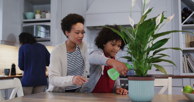 Biracial lesbian couple and daughter watering plants in kitchen. self isolation quality family time at home together during coronavirus covid 19 pandemic.