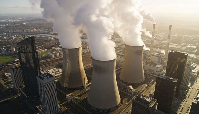 Aerial view of cooling towers emitting steam over power plant and riverside industry