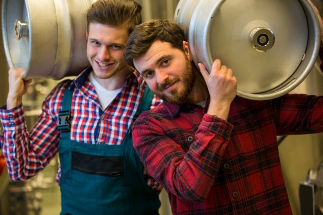 Portrait of brewers carrying keg on shoulder at brewery factory