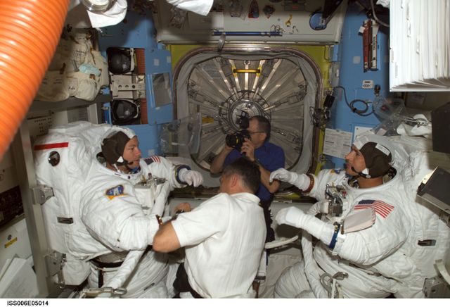 ISS006-E-05014 (28 November 2002) --- Astronaut Paul S. Lockhart, STS-113 pilot, assists astronauts Michael E. Lopez-Alegria (left) and John B. Herrington, STS-113 mission specialists, with their Extravehicular Mobility Unit (EMU) spacesuits in the Quest Airlock on the International Space Station (ISS). Astronaut Donald R. Pettit, Expedition Six NASA ISS science officer, uses a camera in the background.