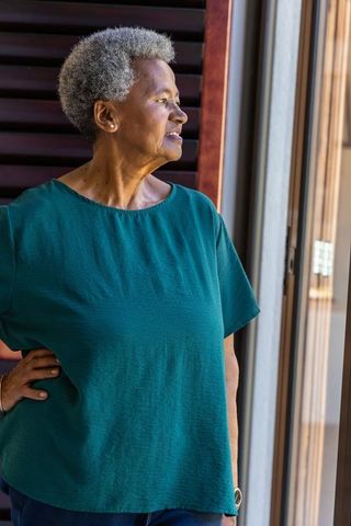 Senior african american woman gazing through sliding glass door at home wearing wristwatch