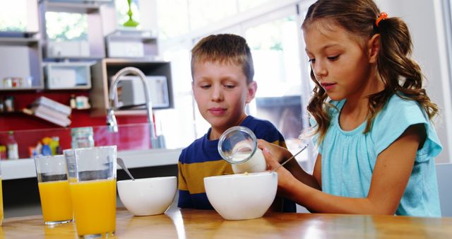 Young boy and girl enjoying breakfast at a kitchen table; perfect for concepts related to healthy eating, family bonding, morning routines, and childhood. Can be used for school projects, nutritional campaigns, or parenting blogs.