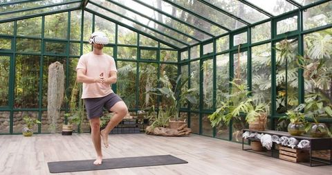 Man Practicing Yoga with VR Headset in Modern Glass House