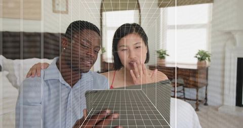 Couple leaning on bed using tablet with 3d wireframe overlay in cozy sunlit modern bedroom