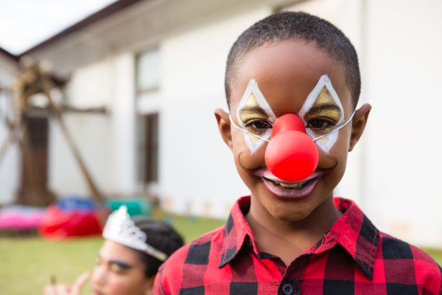 Portrait of boy with face paint wearing clown nose during birthday party in yard