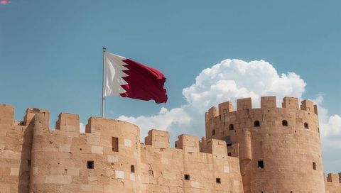 Qatar fortress wall with maroon flag waving over historic sandstone tower