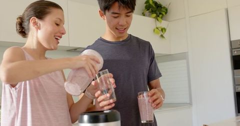 Young couple preparing fresh fruit smoothies in modern kitchen, healthy lifestyle moment
