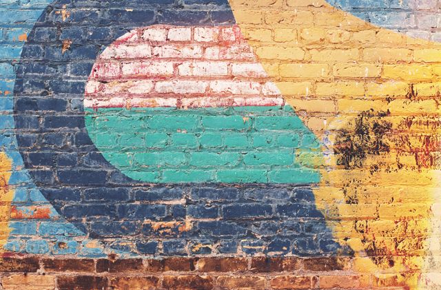 Image shows vibrant abstract graffiti on an old brick wall, mixing green, blue, yellow, and red colors. Ideal for use in articles about urban art, creativity, contemporary street culture, and as background visuals in modern presentations or creative projects.