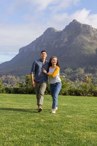 Young couple walking on green lawn with mountain backdrop, enjoying outdoor spring stroll