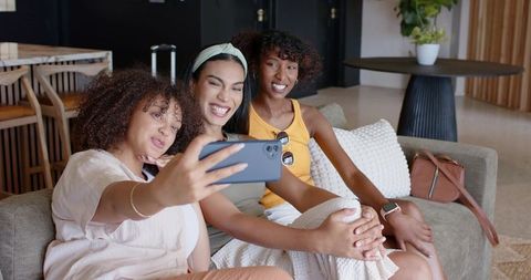 African women friends taking selfie on sofa smiling in modern lounge casual travel-ready vibe