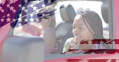 Passenger applying lipstick in red car with flag brushstroke overlay roadtrip mood