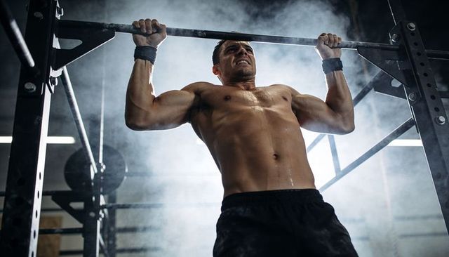 Shirtless male athlete performing pull-up with chalk dust and wrist wraps, intense strength