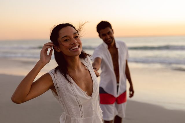 Romantic couple enjoying a beautiful sunset on the beach, holding hands and smiling. Perfect for travel brochures, romantic getaway promotions, lifestyle blogs, and advertisements focusing on love and relationships.