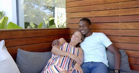 Diverse couple relaxing on outdoor sofa, enjoying quality time