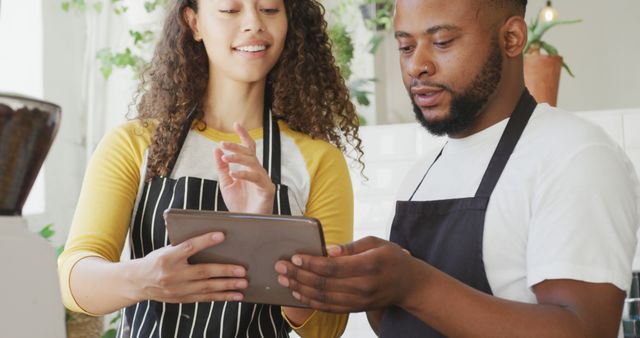 Happy african american male cafe owner and biracial female barista using tablet at cafe. small independent cafe business.