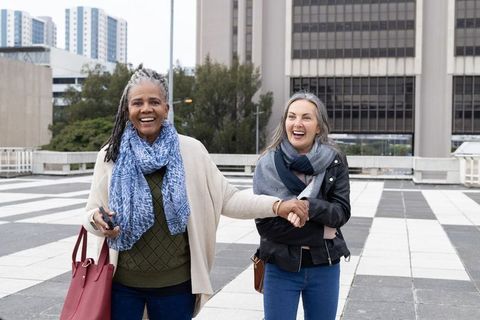 Mature friends walking hand in hand on urban rooftop plaza, laughing during city stroll