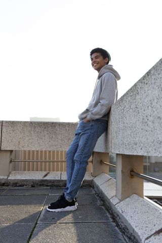 Teen leaning on rooftop parapet smiling in hoodie and beanie urban casual fashion