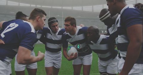 Huddling rugby team preparing for match in misty stadium, wearing navy striped jerseys