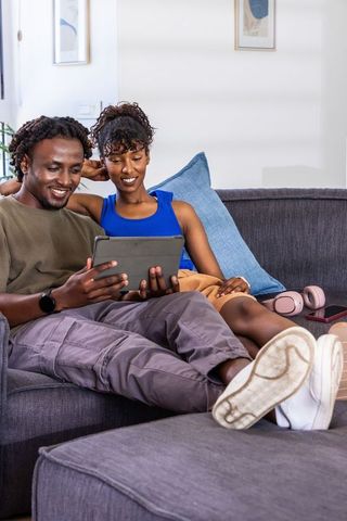 African american couple relaxing on sofa sharing tablet and streaming content at home