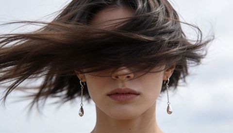 Wind-swept brunette portrait with hair covering face, dangling teardrop earrings