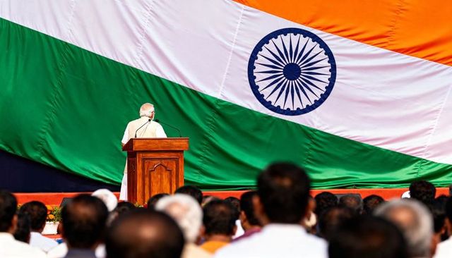 Addressing crowd at podium with giant indian tricolor and ashoka chakra backdrop