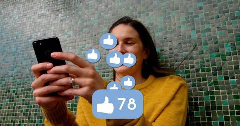 Smiling woman holding smartphone with floating like notifications 78 over mosaic wall