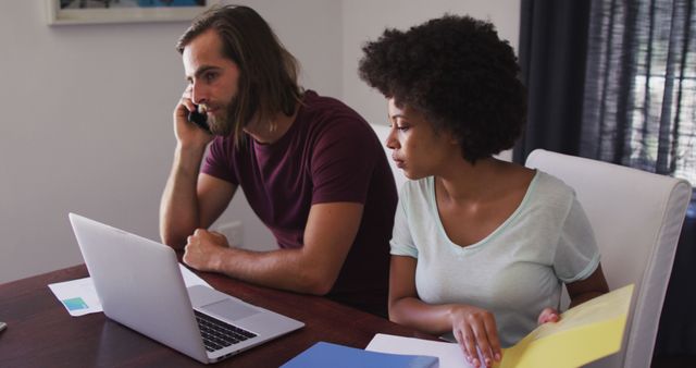 Biracial couple calculating finances and talking on smartphone at home. staying at home in self isolation in quarantine lockdown