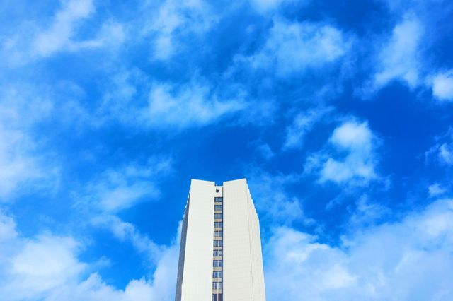 Modern high-rise building set against a vivid blue sky with scattered clouds. Suitable for use in projects related to architecture, urban development, commercial real estate, cityscapes, and modern design themes.