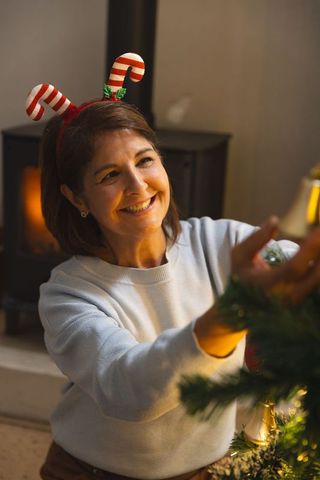 Middle-aged woman decorating christmas tree in cozy home