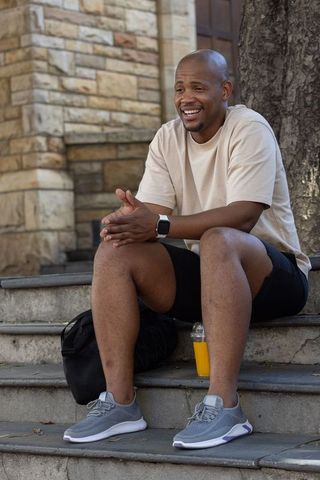 African american man sitting on campus steps with backpack and smartwatch, relaxed casual