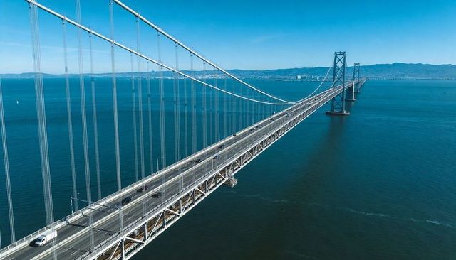 Aerial suspension bridge stretching across deep blue bay with steel cables and light traffic