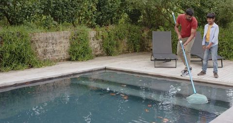 Father and son cleaning pool together in backyard