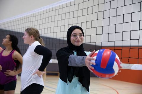 Teenage female volleyball team practicing indoors, hijab player holding red white blue ball