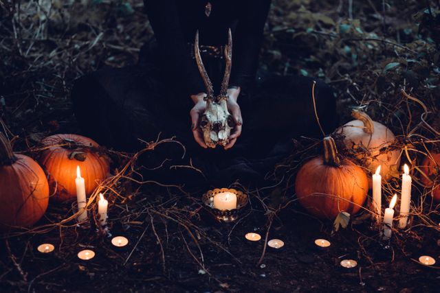 This scene captures a mystical Halloween ceremony in a dark forest. An individual is holding a deer skull, surrounded by lit candles and pumpkins. Natural elements and dim lighting create a spooky, eerie atmosphere perfect for Halloween-themed designs, ritual illustrations, or mysterious autumn storytelling.